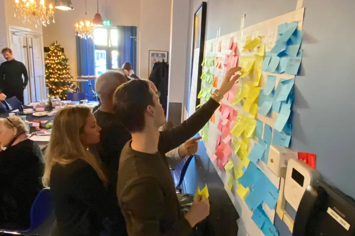 Medewerkers werken samen tijdens een brainstormsessie met kleurrijke post-its op een muur, wat een levendige bedrijfscultuur en samenwerking illustreert.